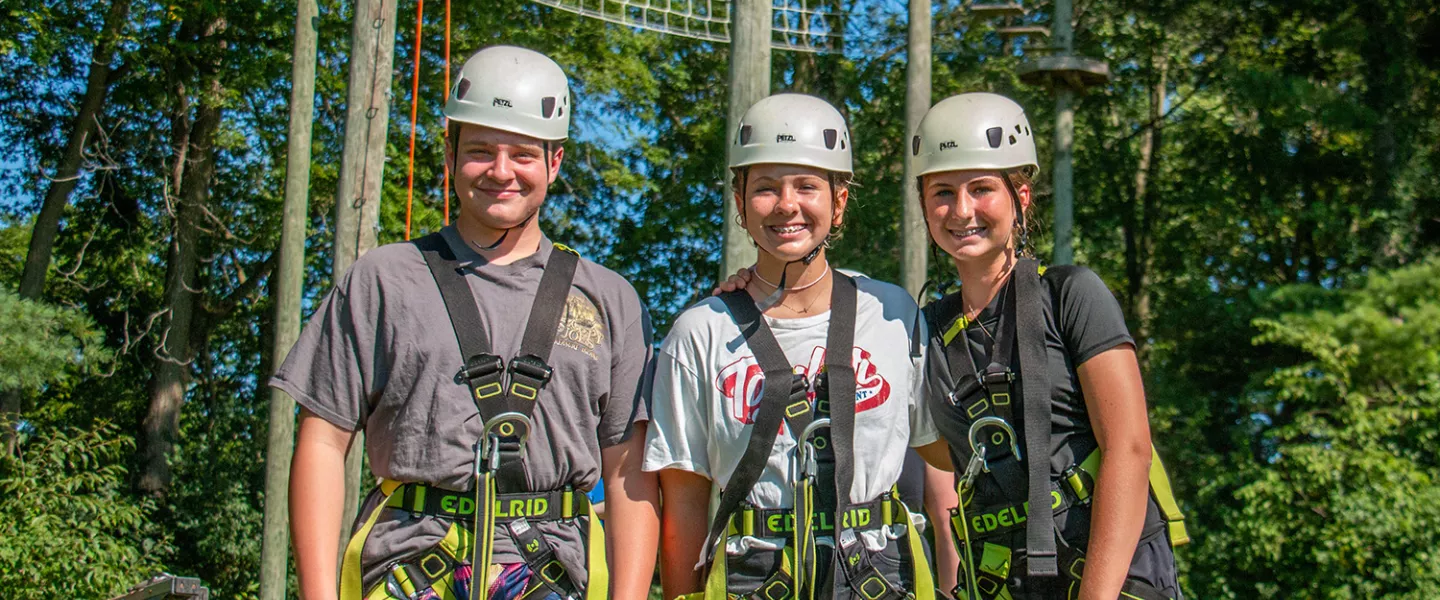 Campers in safety equipment smiling in front of high ropes course