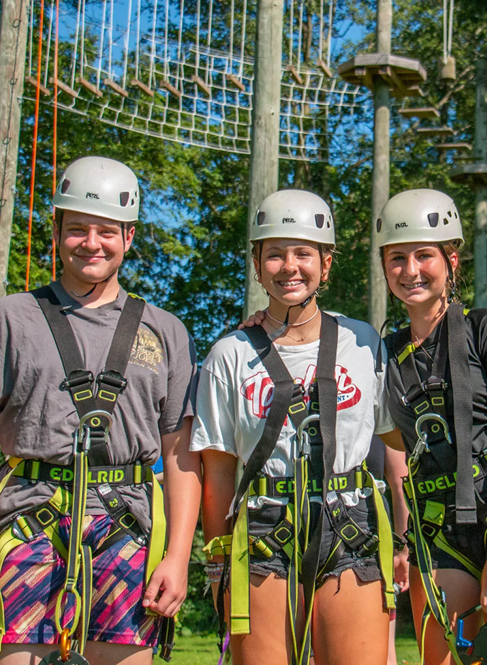 Campers in safety equipment smiling in front of high ropes course