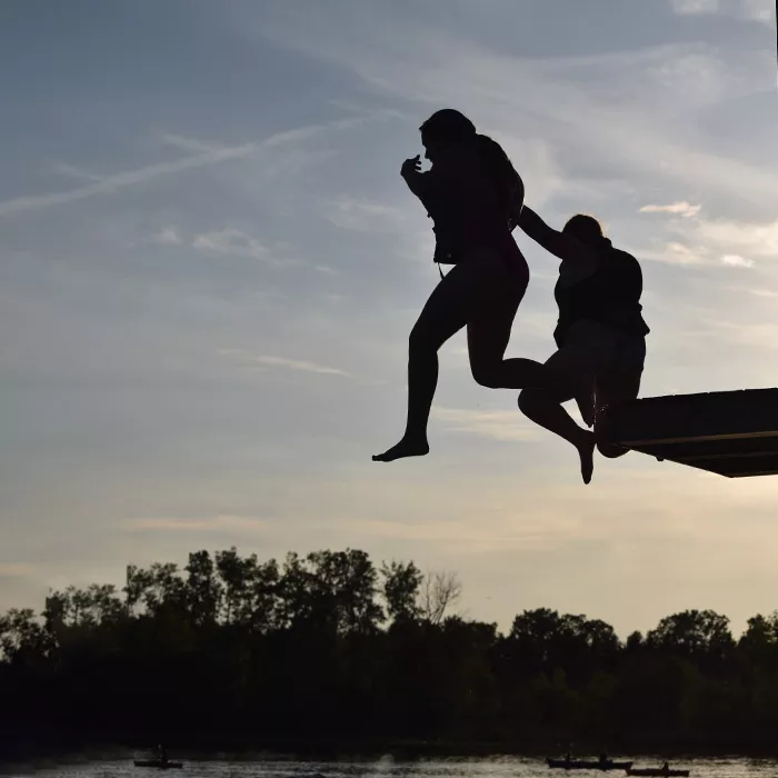 Two campers jumping off the high dive into the lake