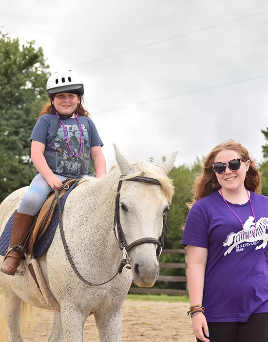 Camper riding a horse with staff walking along side