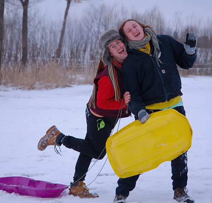 Two campers smiling with sleds in the snow